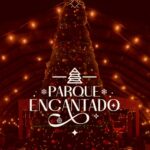 A imagem mostra uma grande árvore de Natal iluminada, decorada com bolas coloridas e luzes douradas. Ela está posicionada no centro de um espaço coberto, com várias luzes penduradas no teto em formato de fios, criando um clima aconchegante e festivo. No centro da imagem, sobre a árvore, há um logotipo branco com o desenho estilizado de uma árvore de Natal e o texto “Parque Encantado” em letras elegantes. O fundo é em tons quentes e avermelhados, transmitindo uma sensação natalina e mágica.